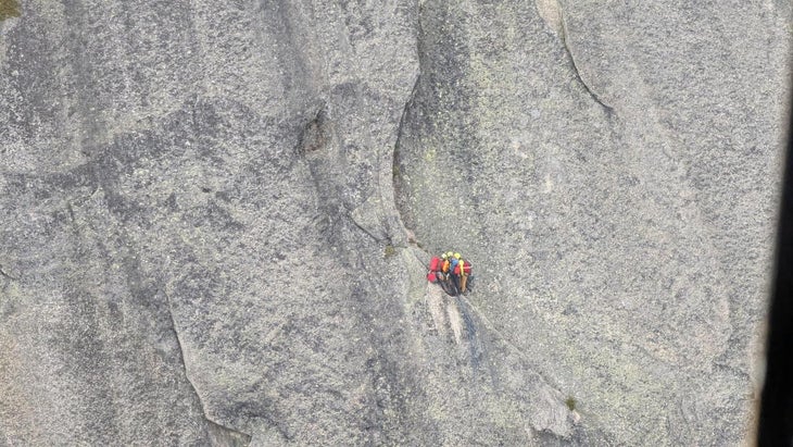 Two Search and Rescue responders tend to injured climber partway up a cliff.